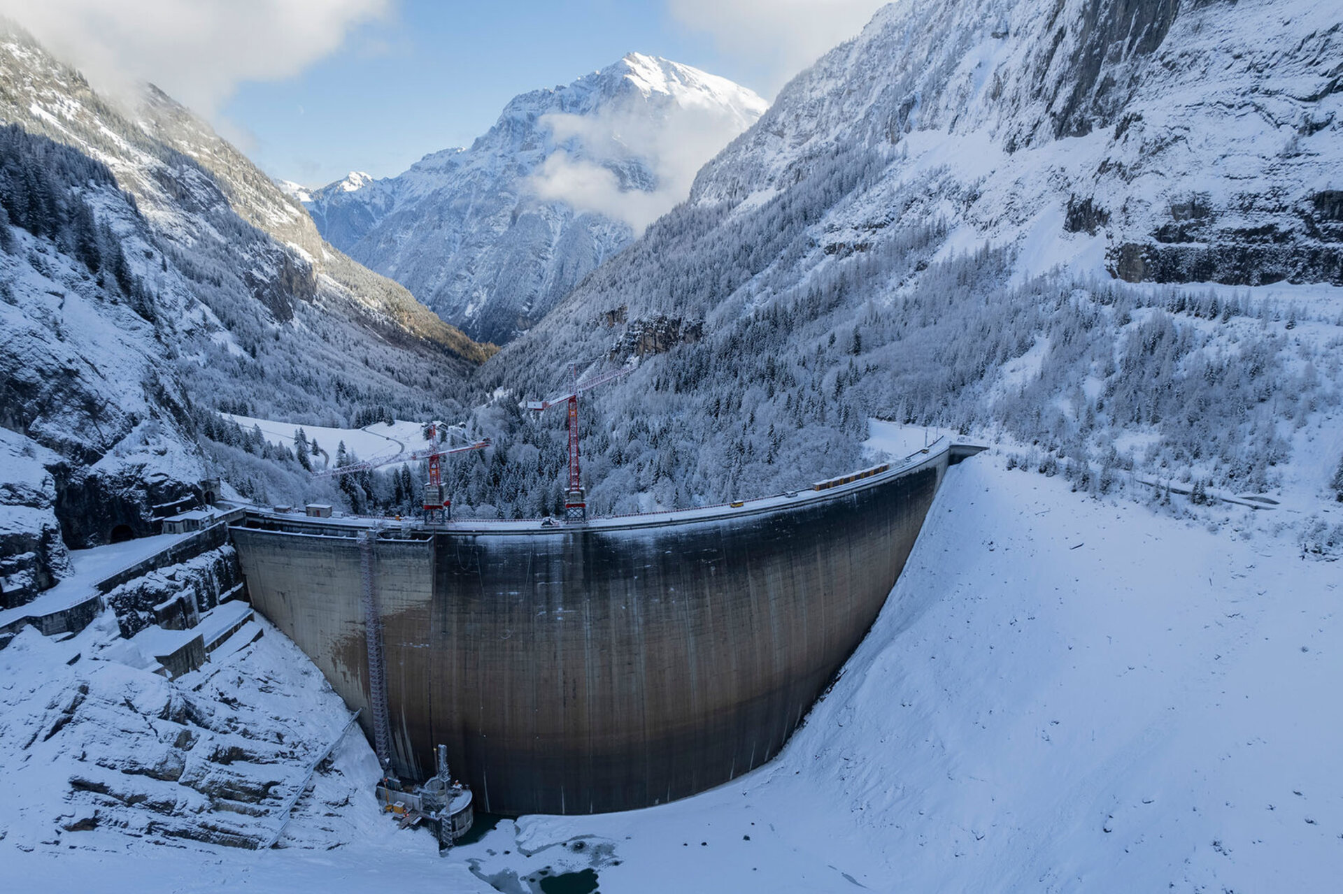 Vue aerienne du barrage de Gigerwald (Axpo) dans une vallee alpine hivernale - montagnes et sapins enneiges entourant le lac de Gigerwald et le grand barrage en beton