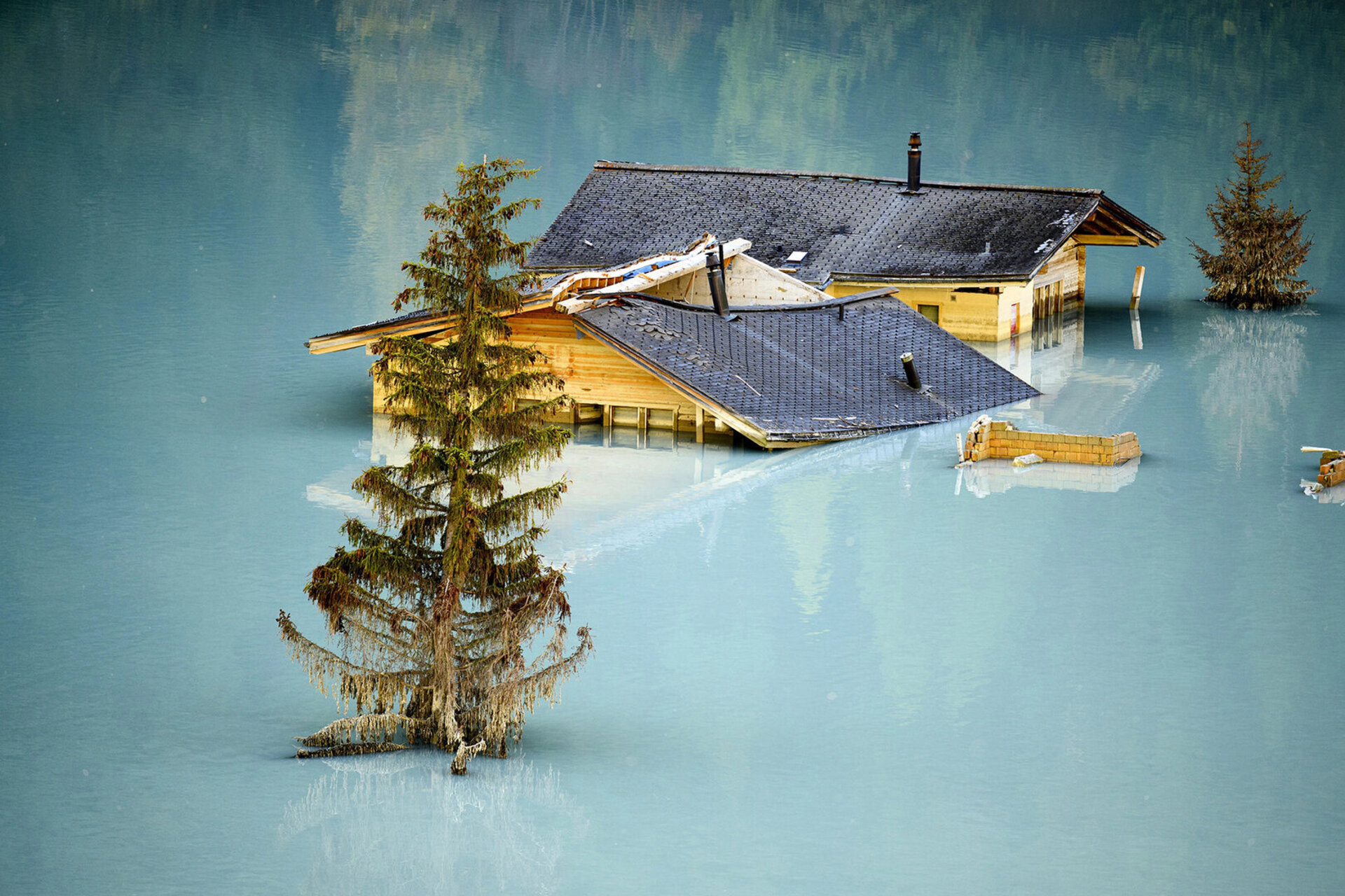 1. Preis Aktualität/Actualité/Attualita/News: LAURENT GILLIERON - BLATTEN 2030 - Trois mois et demi après le glissement de terrain dévastateur de Blatten (VS), les stigmates de l’ensevelissement du village du Lötschental demeurent visibles. Les maisons détruites se dressent dans un lac artificiel formé par l’accumulation des débris. En ce 19 septembre, le regard se tourne vers l’avenir : le premier coup de pioche symbolique est donné pour le projet de reconstruction « Blatten 2030 ».