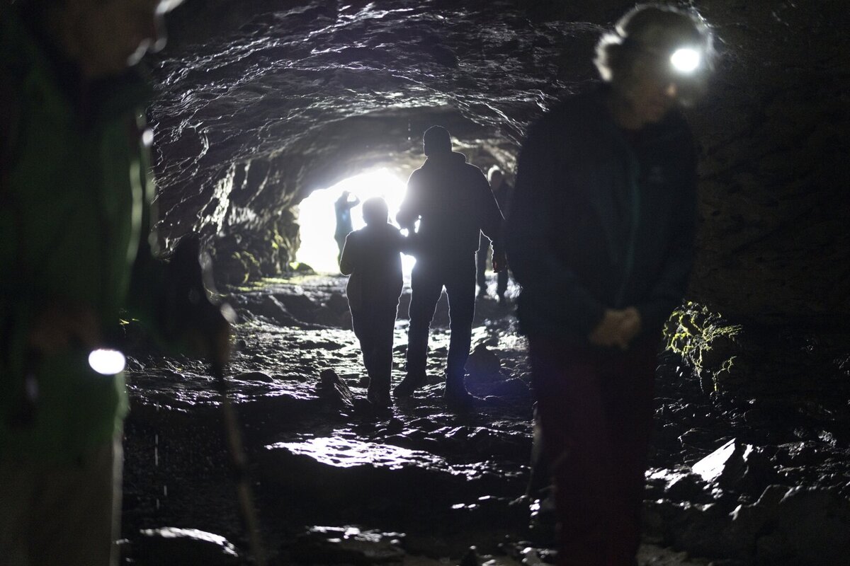Silhouetten von Besucherinnen und Besuchern mit Stirnlampen im Hoehlengang des Drachenlochs im Taminatal.