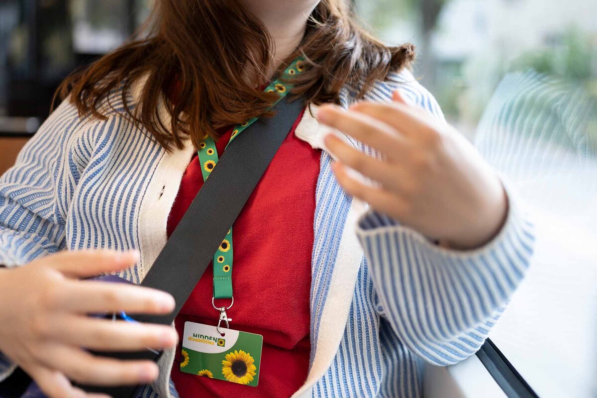 Eine Person reist im oeffentlichen Verkehr mit einem -Hidden Disabilities- Ausweis an einem Schluesselband mit Sonnenblumen (Sunflower Lanyard).
