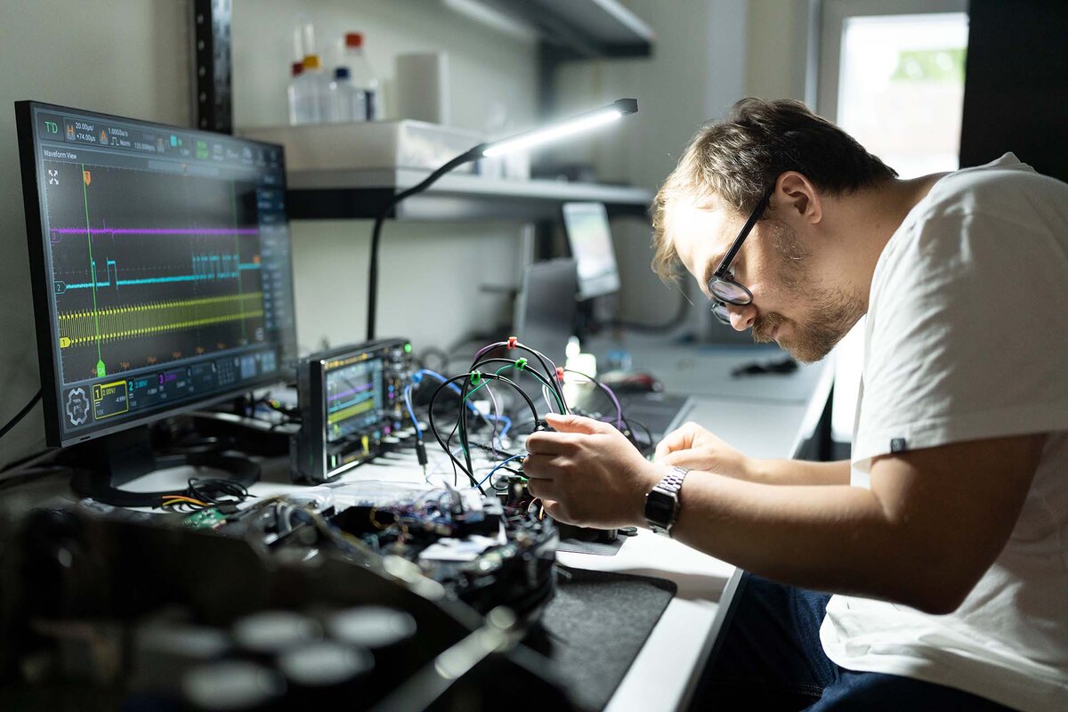 Ein ethical Hardware-Hacker analysiert ein eingebettetes Geraet eines geoeffneten, aber funktionierenden Smart-Staubsauger-Roboters, fotografiert im Labor des Nationalen Testinstituts fuer Cybersicherheit (NTC).