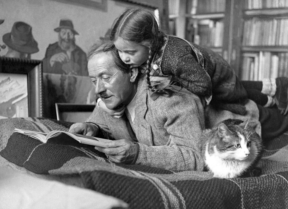 Der Maler Albert Nyfeler (1883-1969), aufgenommen in Kippel im Loetschental bei der Lektuere mit seiner Tochter Rea Nina genannt Rehli, im Beisein einer Katze.