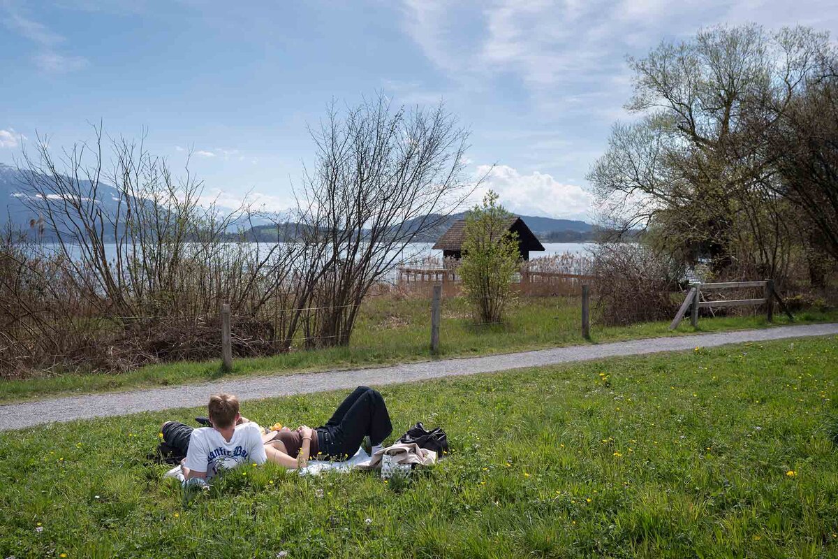 Junge Menschen liegen im Gras am Seeufer des Zugersees auf der Lorzenebene, zwischen Cham und der Stadt Zug, fotografiert am Montag, 6. April 2026 in Zug. Die Stiftung Landschaftsschutz Schweiz SL zeichnet die Lorzenebene bei Zug als Landschaft des Jahres 2026 aus. 