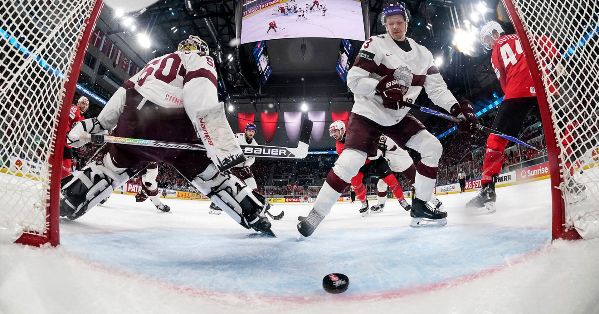 Switzerland's Damien Riat, back middle, scores the third goal against Latvia's goaltender Kristers Gudlevskis, left, and Latvia's Alberts Smits, right, during the 2026 IIHF Men's Ice Hockey World Championship preliminary round group A game between Switzerland and Latvia