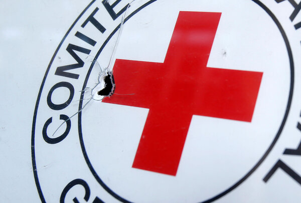 Nahaufnahme eines Schildes des Roten Kreuzes mit rotem Kreuzsymbol, das von einem Einschussloch und Rissen im Material beschädigt ist.