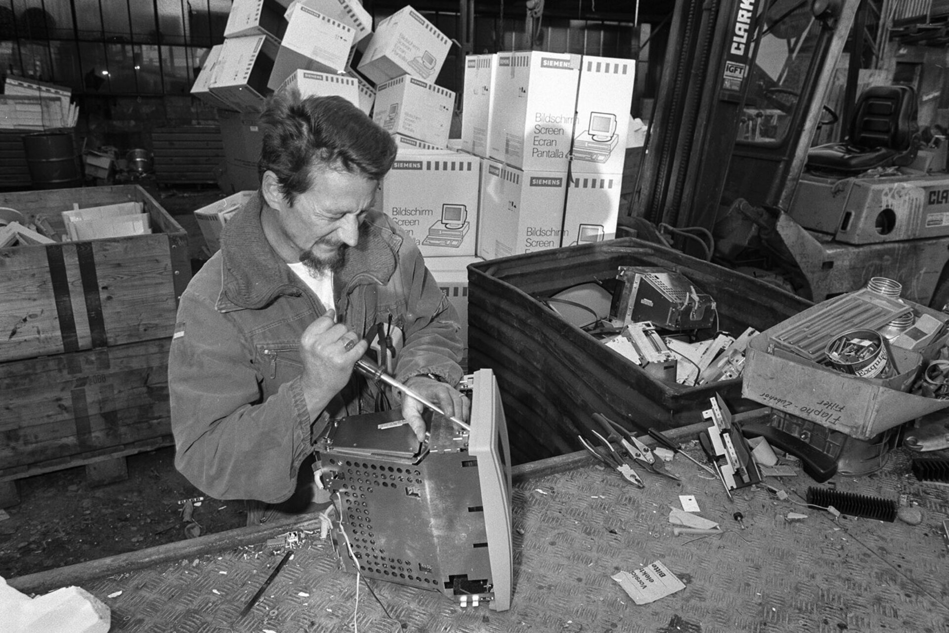 Un homme demonte un ancien ecran d'ordinateur avec un tournevis dans un atelier ou un centre de recyclage.