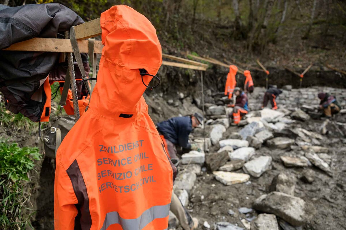 Die Jacke eines Zivildienstleistenden haengt neben der Baustelle einer Trockenmauer.