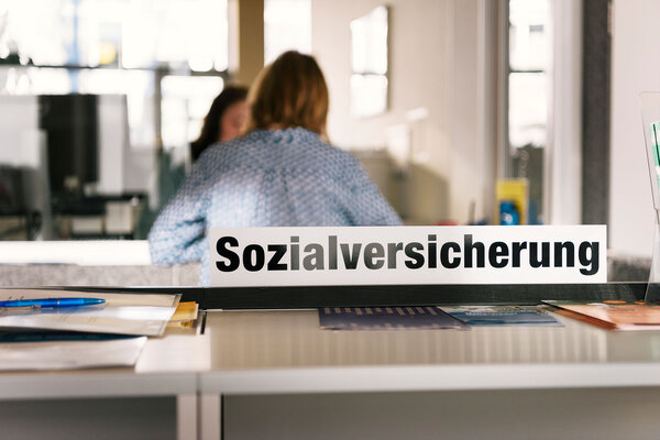 A sign which reads 'Sozialversicherung' (English: social insurance) and people pictured talking at a counter in the counter hall of the social center Albisriederhaus on Albisriederstrasse in Zurich