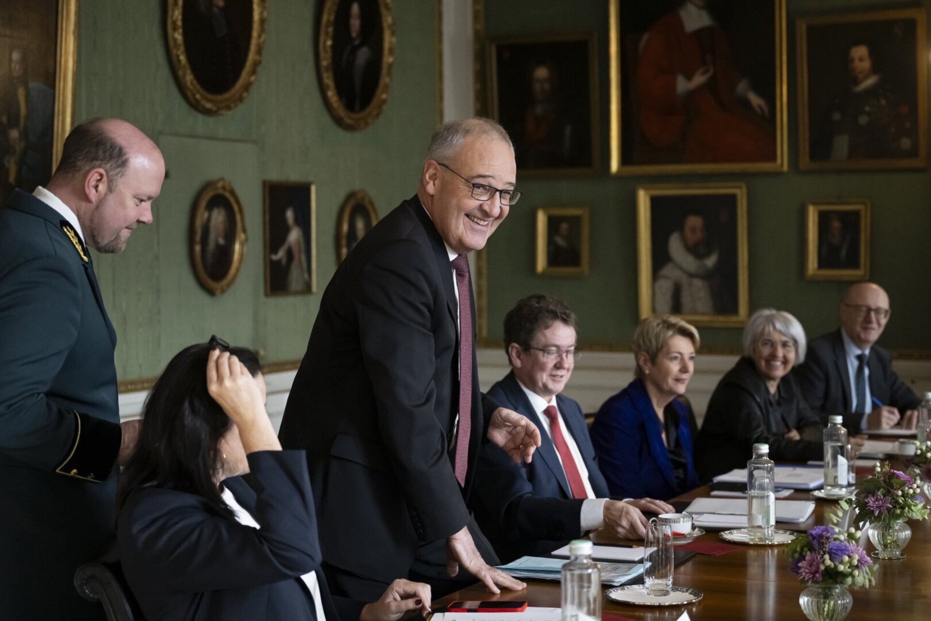 Le conseiller federal Guy Parmelin se tient a la table de reunion et sourit lors des entretiens de Von-Wattenwyl, d'autres membres du Conseil federal sont assis a cote de lui dans une salle historique a la Maison de Von-Wattenwyl.