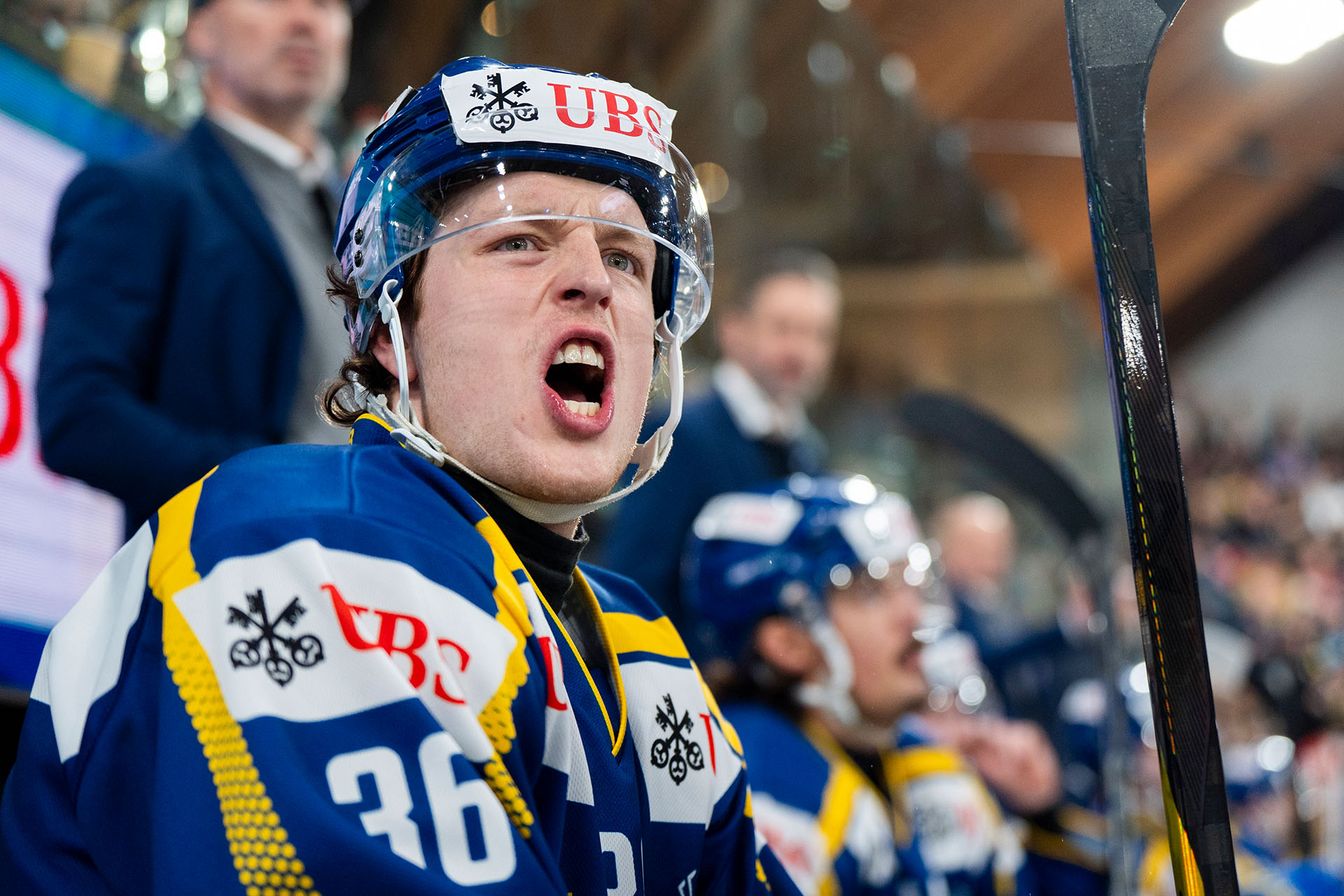 Un joueur de hockey sur glace sur le banc crie pendant un match de la Coupe Spengler a Davos, casque et maillot avec le logo UBS.