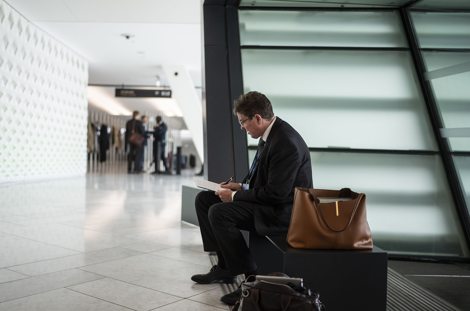 Le conseiller federal Albert Roesti est assis sur un banc dans un batiment moderne et prend des notes sur une feuille de papier.