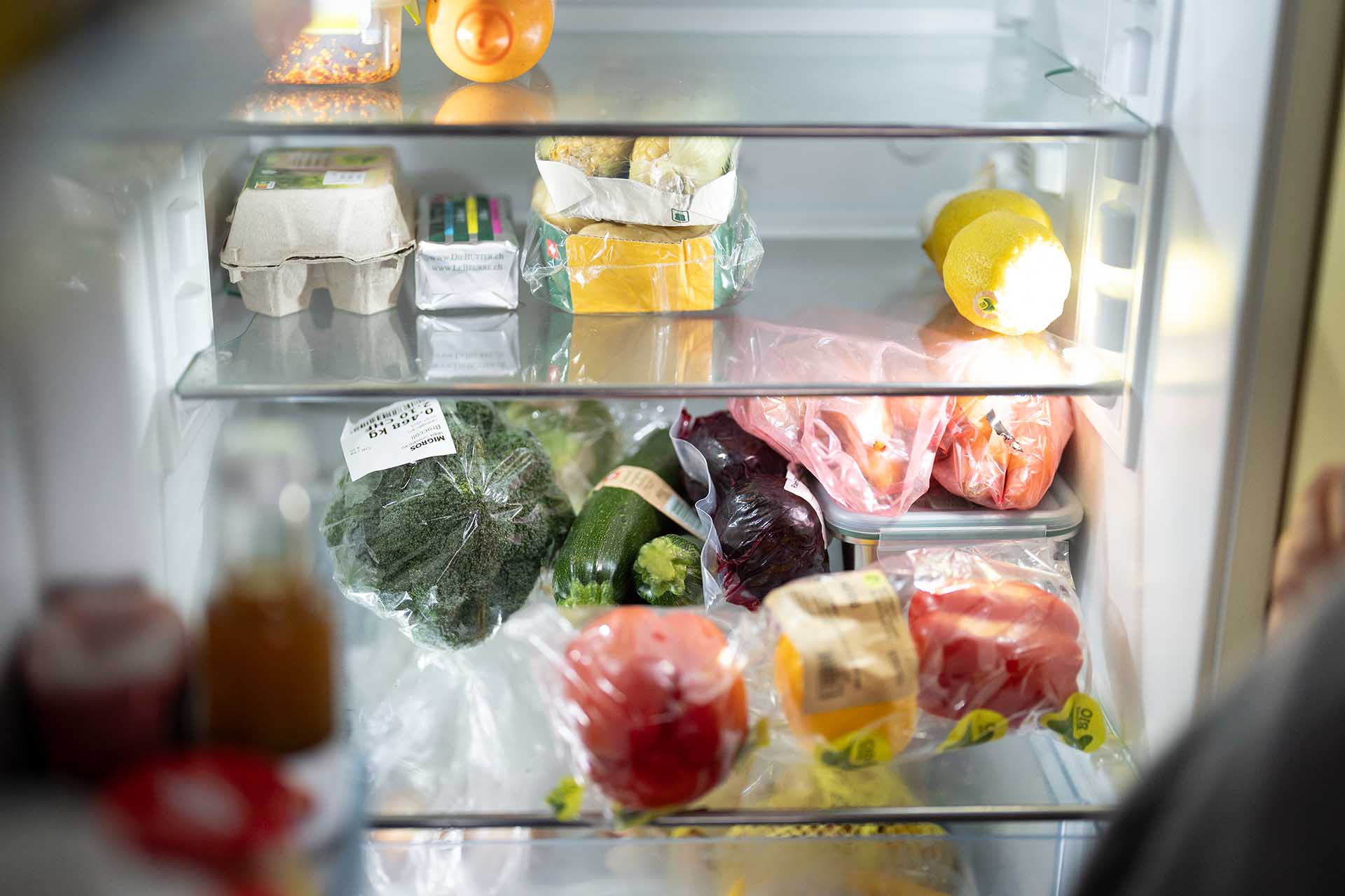 Vue dans un refrigerateur avec des oeufs, du fromage, des citrons et divers legumes et fruits emballes sur les etageres.